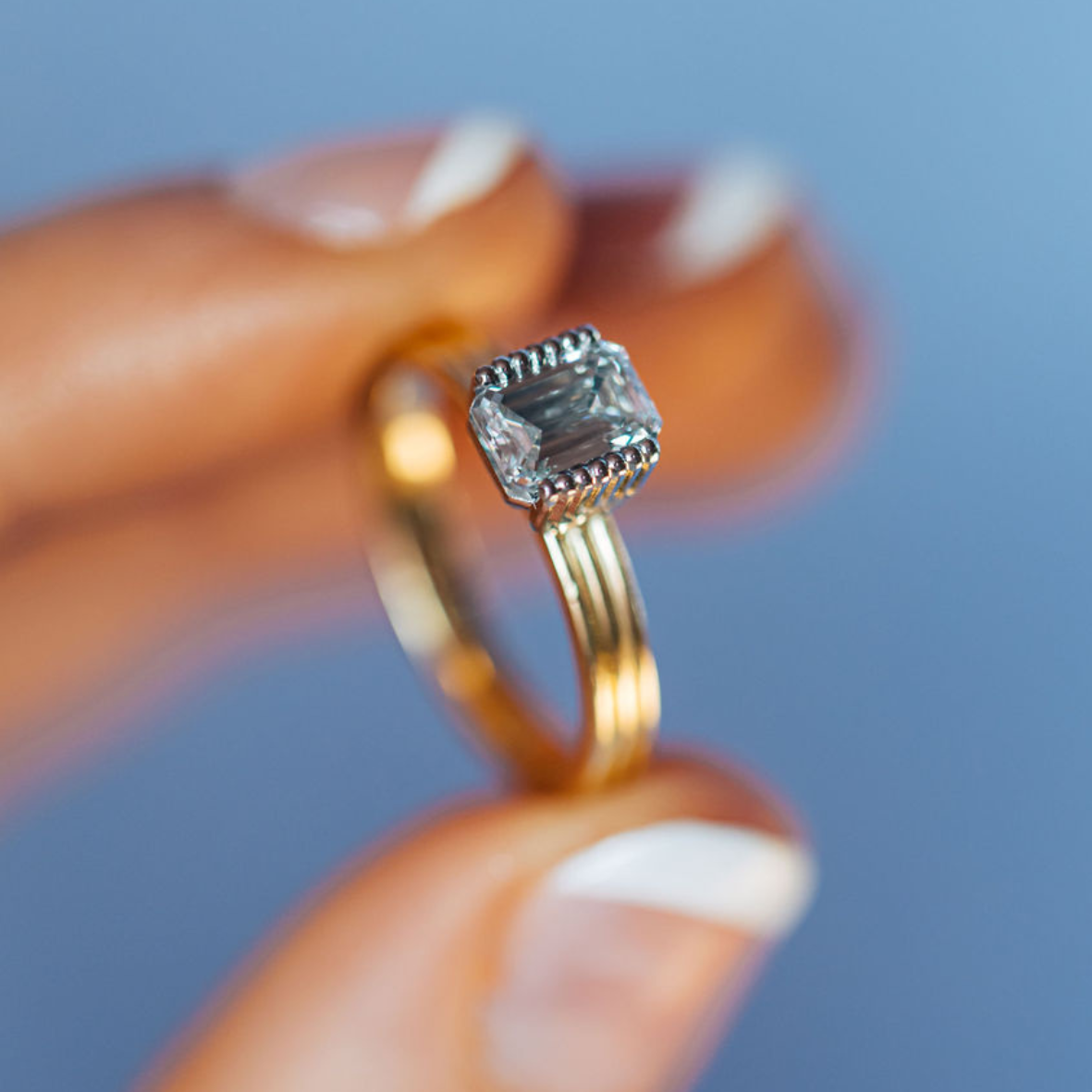 Close up of yellow gold ring with emerald cut diamonds being held by a persons hand
