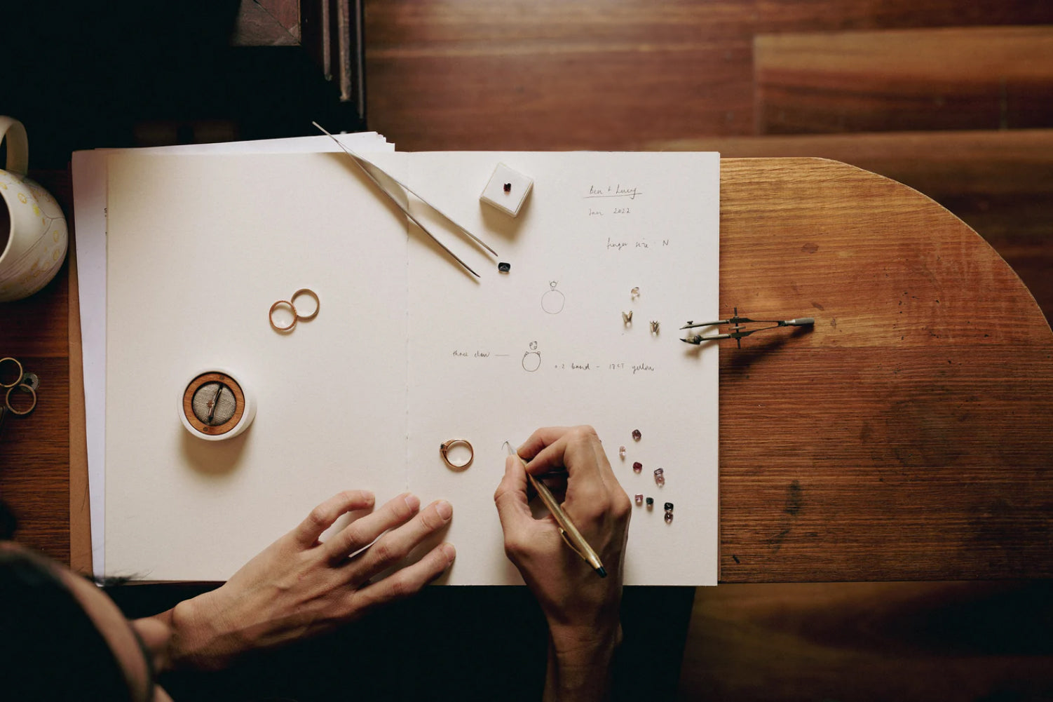 Person working on jewelry design with tools and materials on a wooden table