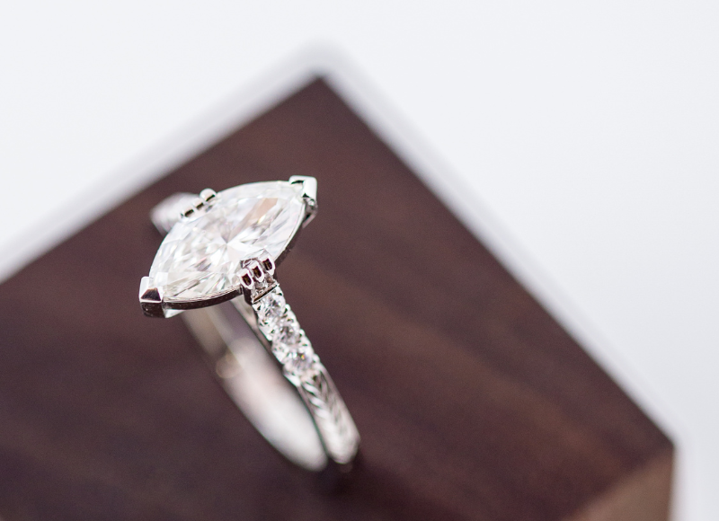 Close up of a diamond ring with a marquise-shaped center stone on a wooden stand.